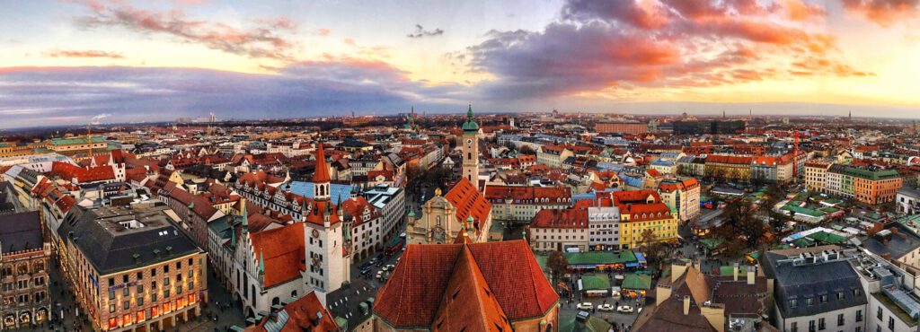 Luftaufnahme der Münchner Innenstadt mit historischen Kirchen, roten Dächern und urbaner Bebauung im Abendlicht