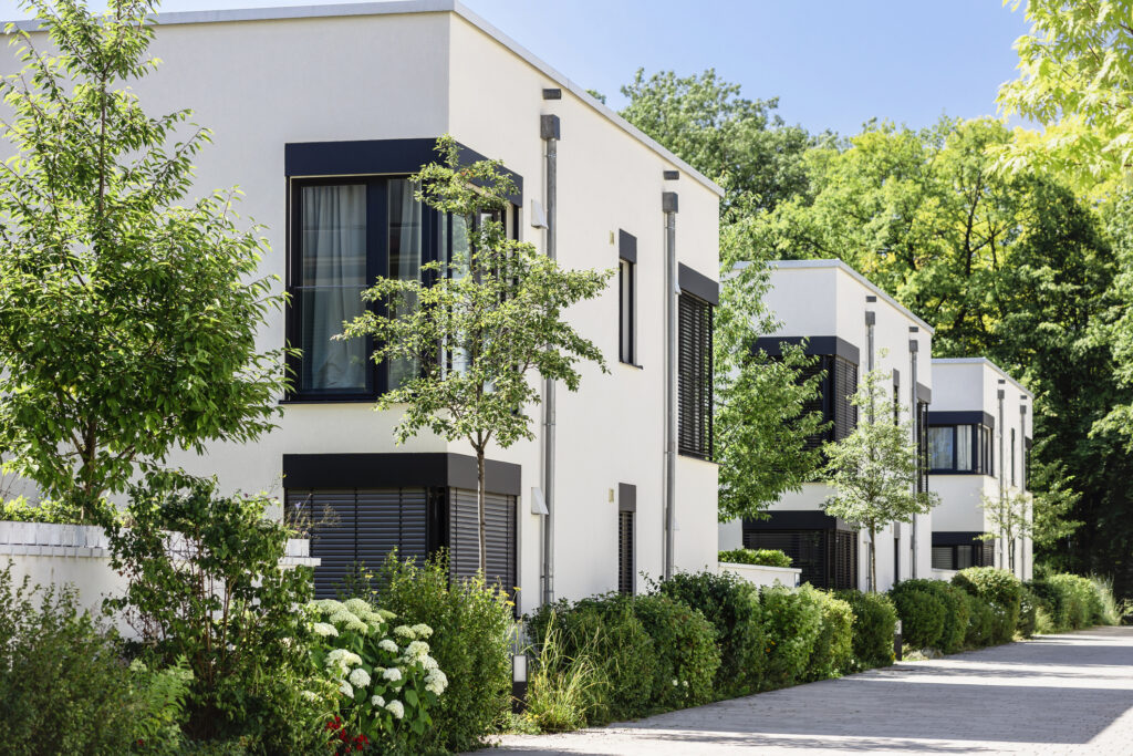 Moderne Reihenhäuser mit weißer Fassade und großen Fenstern in grüner Wohnanlage