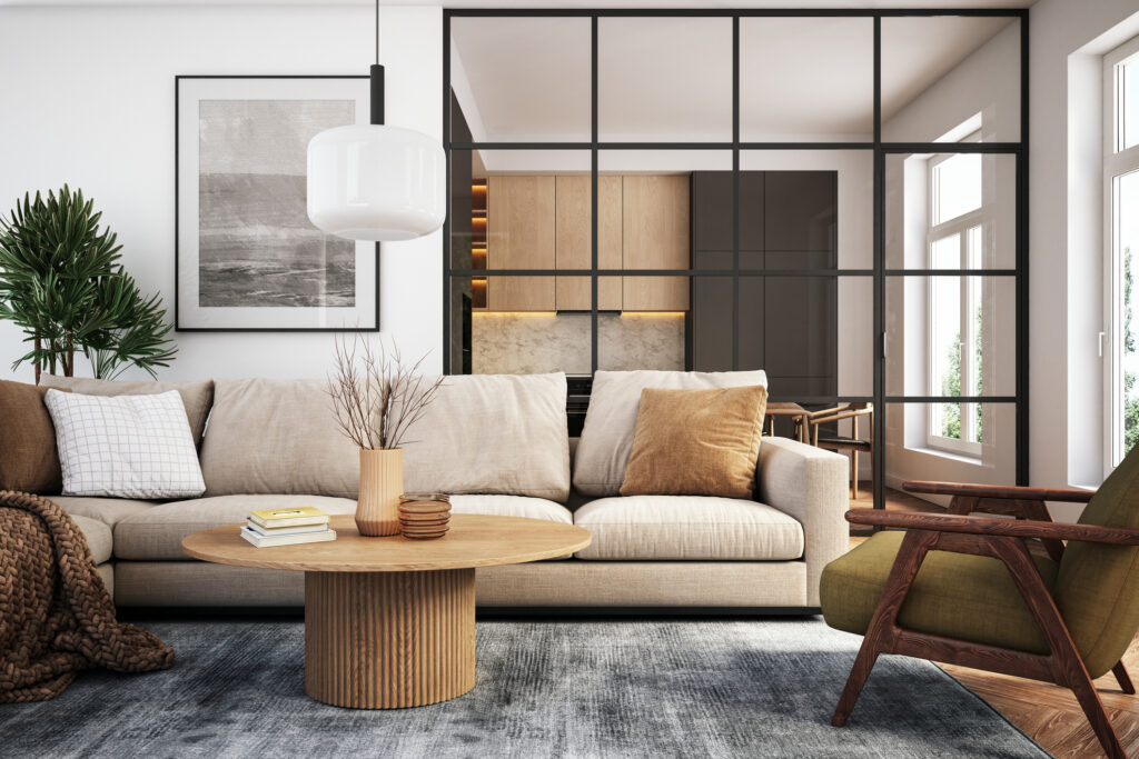 Wohnzimmer mit beigem Sofa, dekorativen Kissen, rundem Tisch und bodentiefer Glaswand vor offener Küche