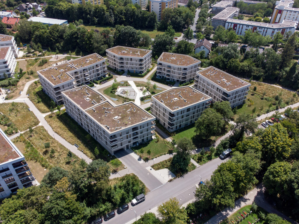 Moderne Wohnsiedlung aus der Vogelperspektive, umgeben von Bäumen, Straßen und weiteren Gebäuden.