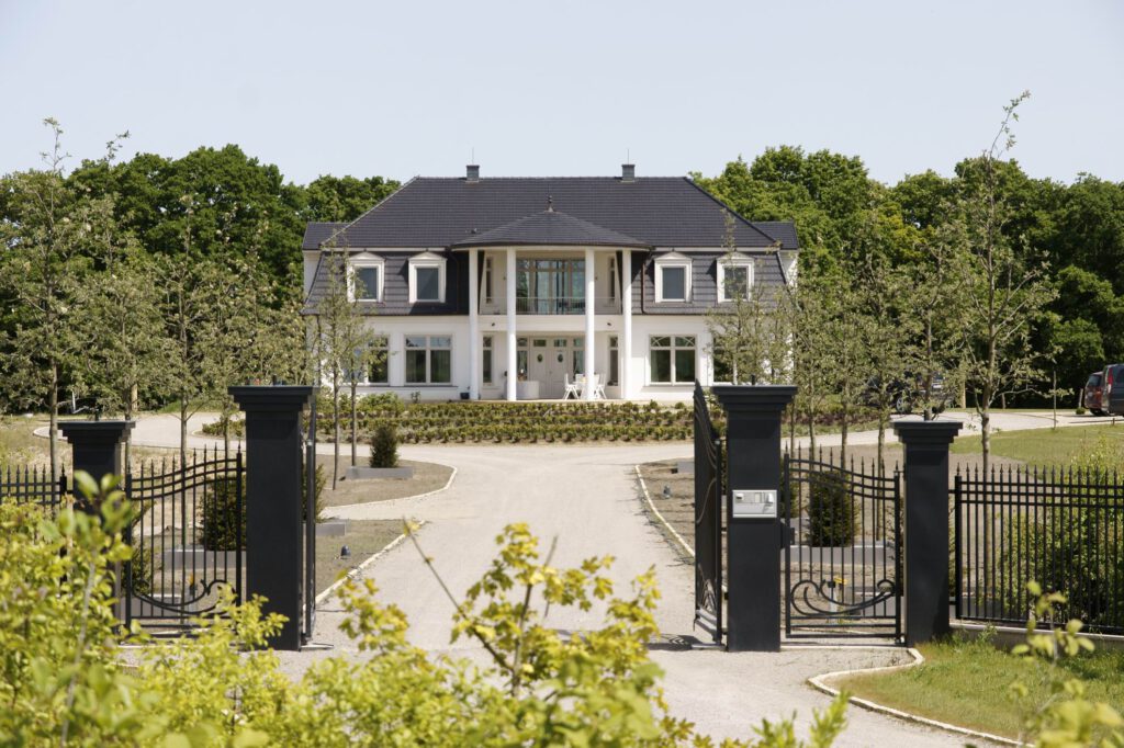 Weiße Villa mit großer Auffahrt, Garten und schwarzem Einfahrtstor.