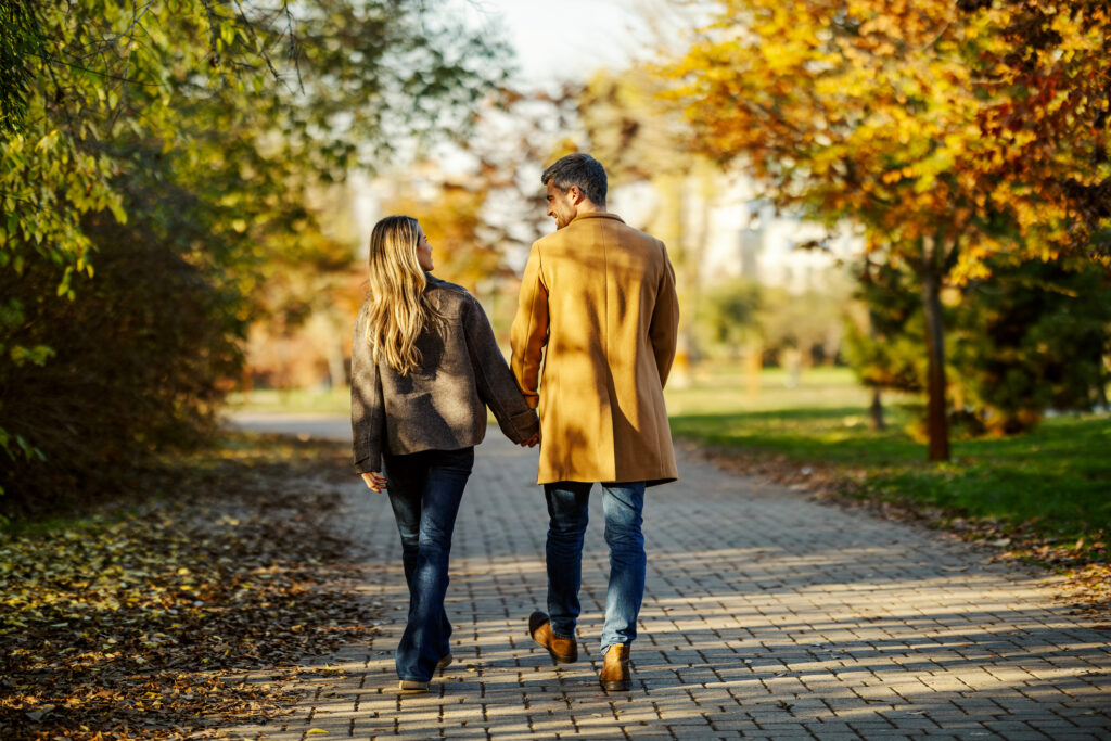 Spaziergang im Park mit zwei Erwachsenen auf einem Weg, umgeben von Bäumen mit Herbstlaub